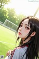 A girl with long black hair standing in front of a soccer field.