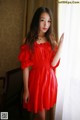 A woman in a red dress leaning against a window.