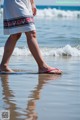 A woman walking on the beach with her feet in the water.