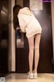 A woman in a white hoodie and white tights standing in front of an elevator.