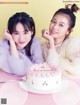 A couple of women sitting next to each other near a cake.